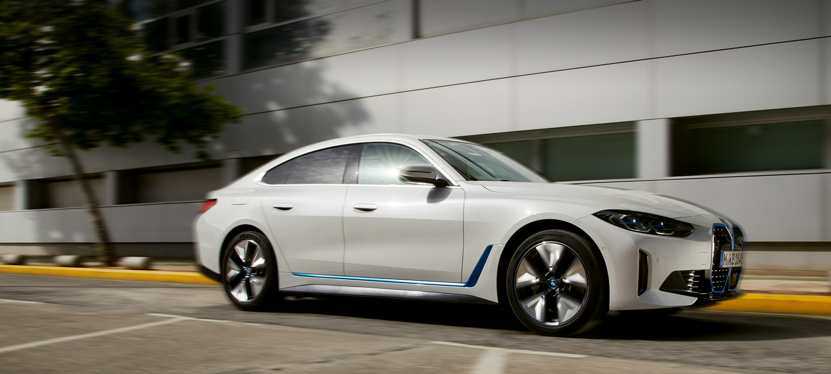 BMW i4 eDrive40 G26 2021 three-quarter side view driving in front of building BMW i4 eDrive40 G26 2021 three-quarter side view driving in front of building