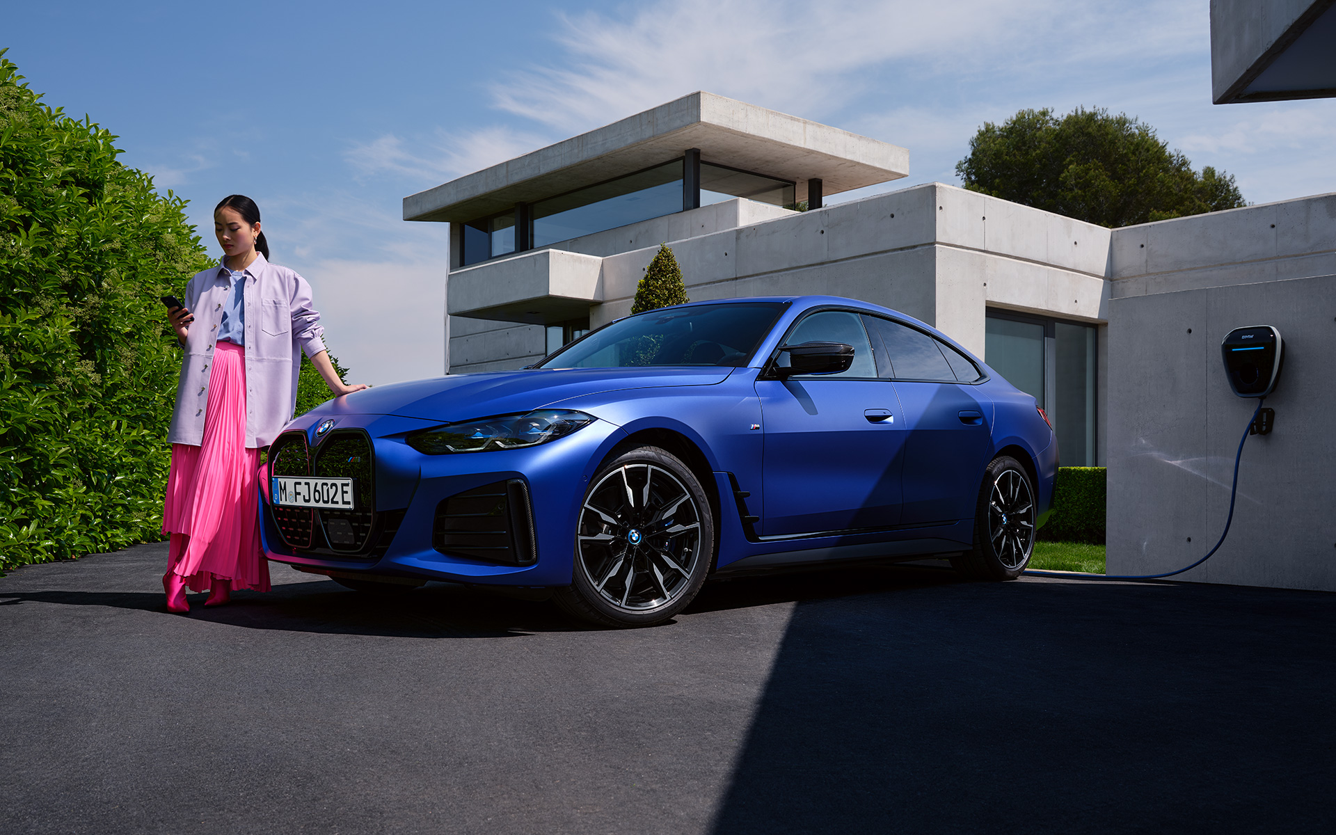 BMW i4 M50 G26 2021 BMW Individual Frozen Portimao Blue metallic three-quarter front view standing with woman in front of house