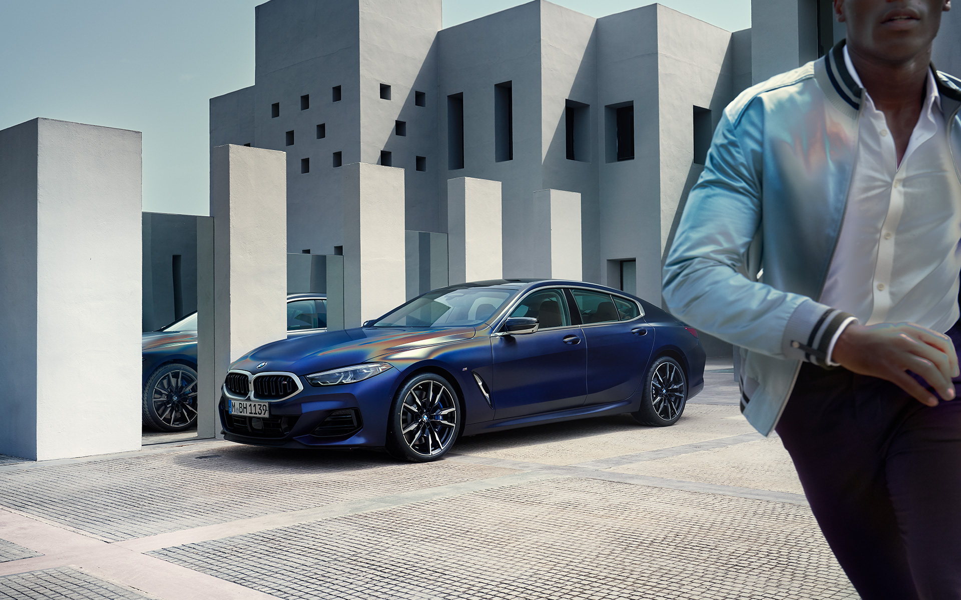 Three-quarter front view BMW M850i xDrive Gran Coupé G16 LCI Facelift 2022 BMW M850i xDrive Gran Coupé G16 LCI Facelift 2022 BMW Individual Frozen Tanzanite Blue metallic three-quarter front view standing with male model in foreground