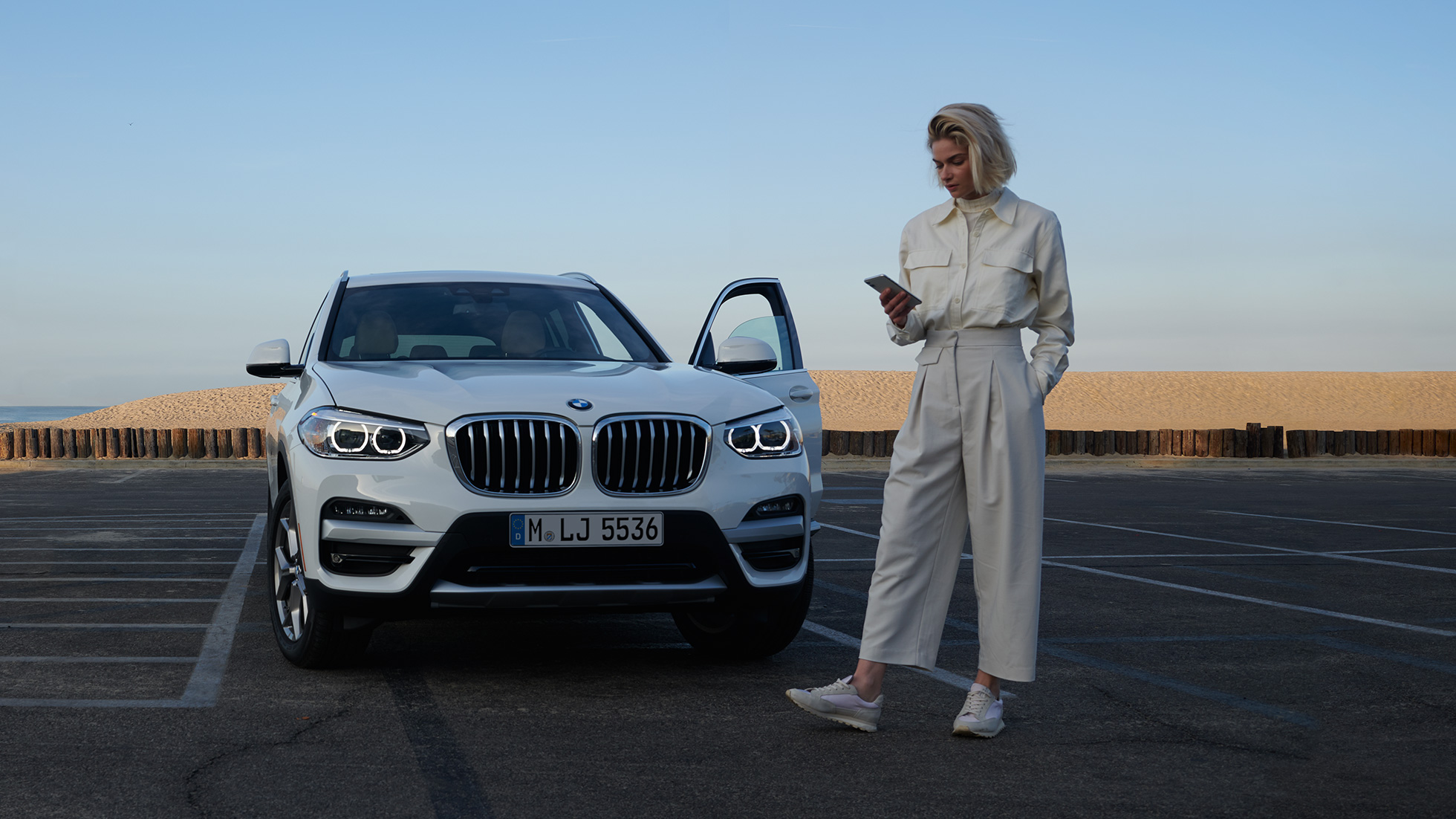 Woman using My BMW App on smartphone Woman using My BMW App from BMW ConnectedDrive on smartphone in front of a white BMW X5