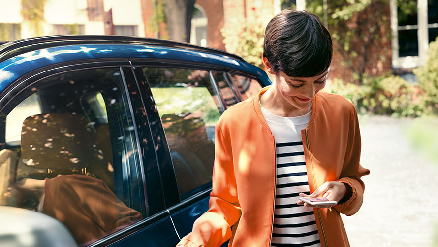 BMW Teleservices BMW Teleservices: woman stand in front of BMW and uses smartphone